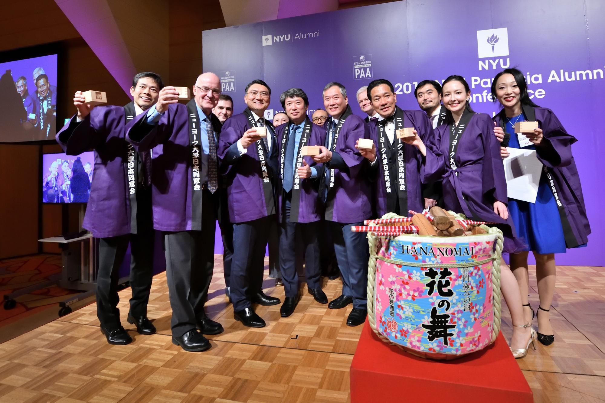 Former NYU President Andrew Hamilton with NYU Trustee Andre Koo and attendees in Tokyo holding a gift