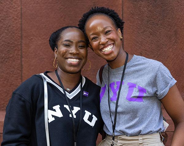 Two alumni smiling in front of Bobst