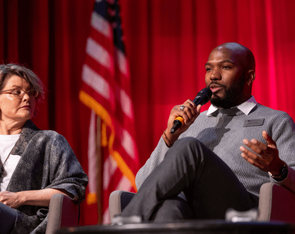A panelist talking with a mic in front of a red curtain