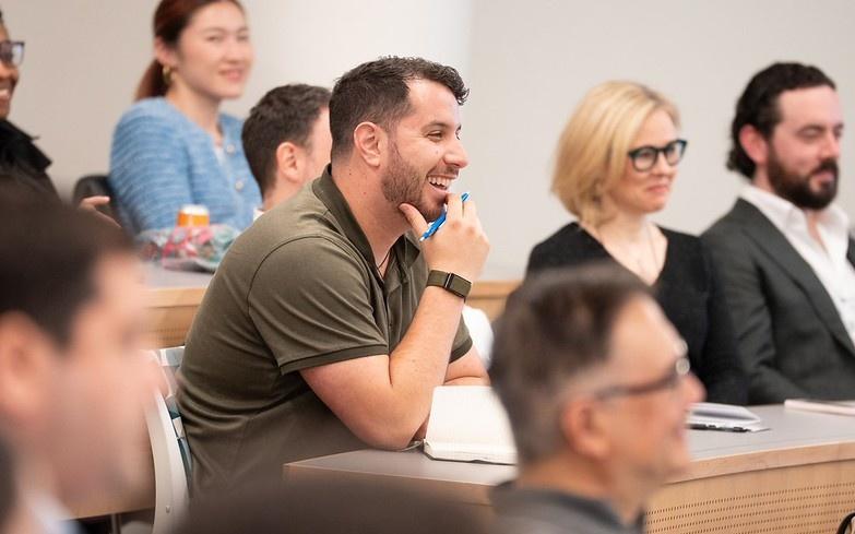 alumnus smiling in a classroom with a notebook and a pen