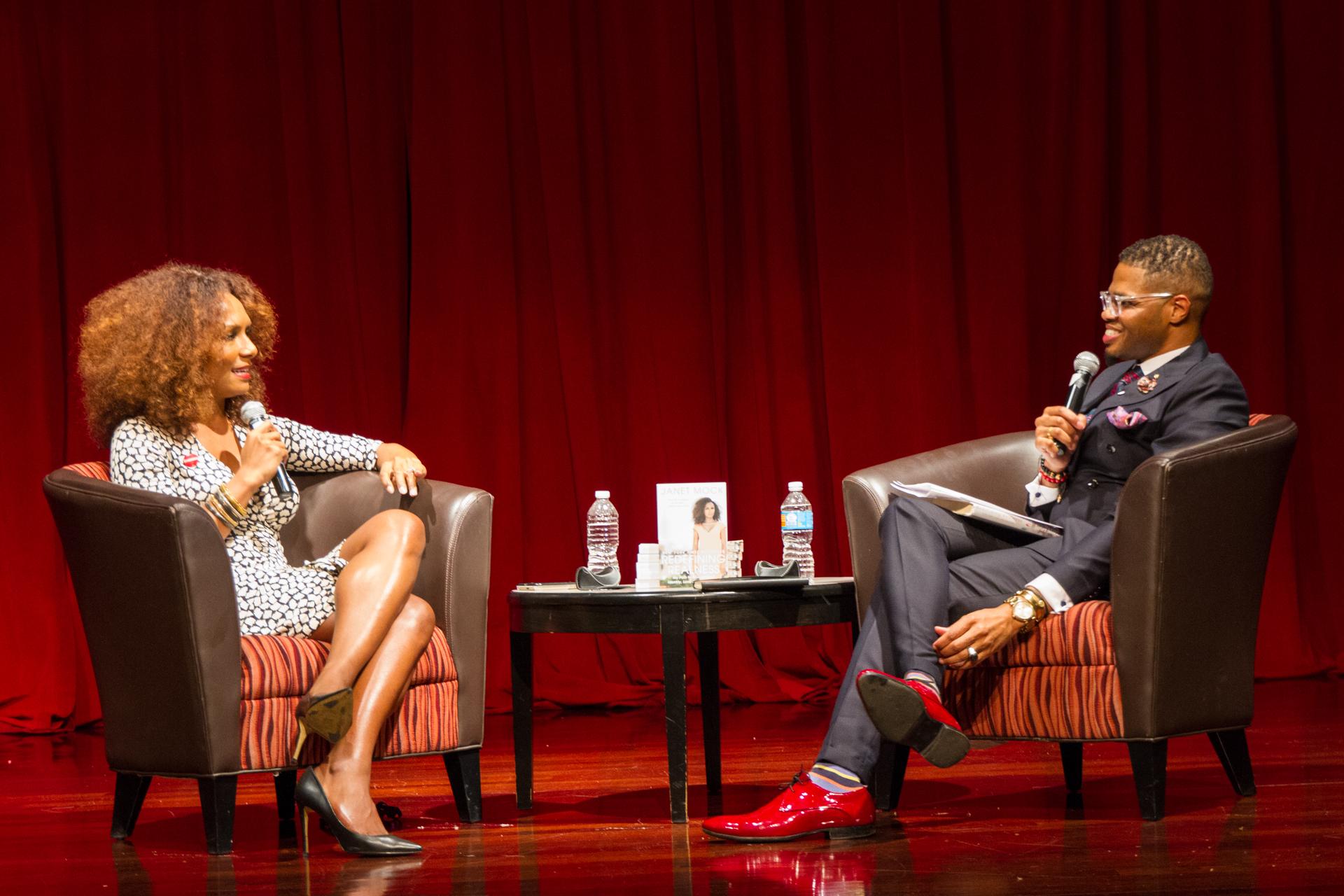 A conversation between two people on a stage with a red curtain